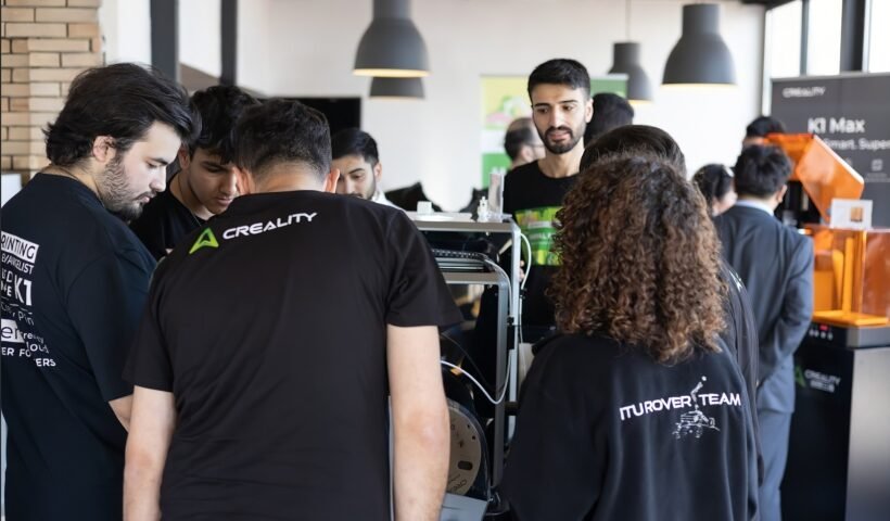 Creality logolu tişört giyen katılımcılar bir 3D yazıcıyı yakından incelerken