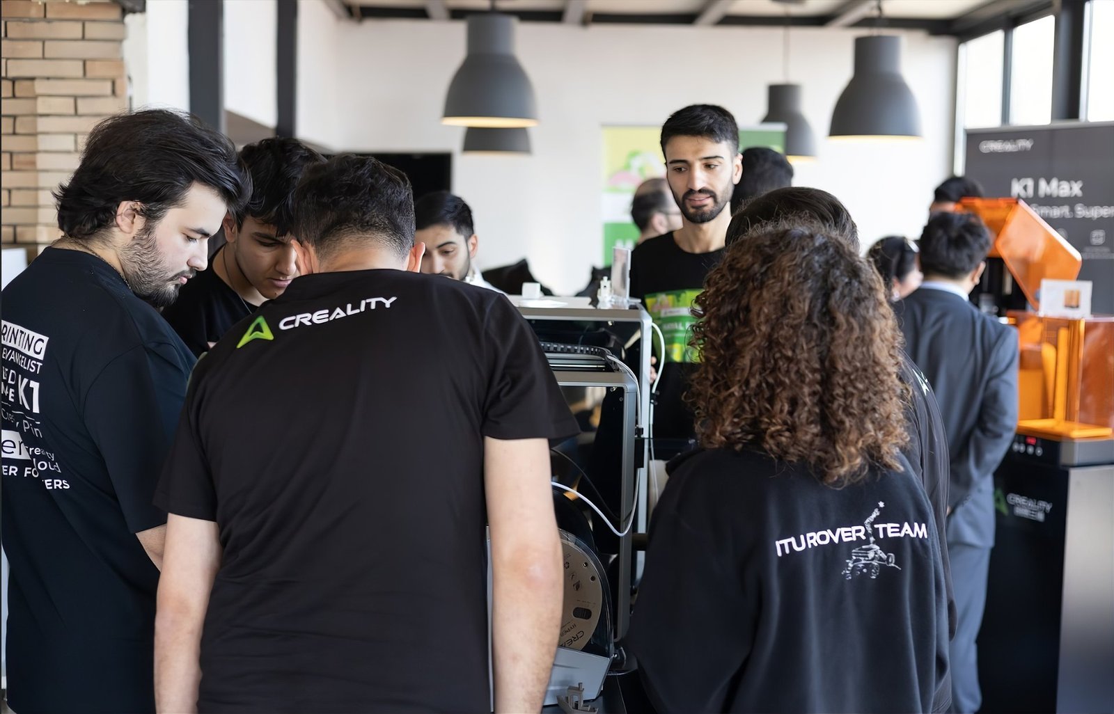 Creality logolu tişört giyen katılımcılar bir 3D yazıcıyı yakından incelerken