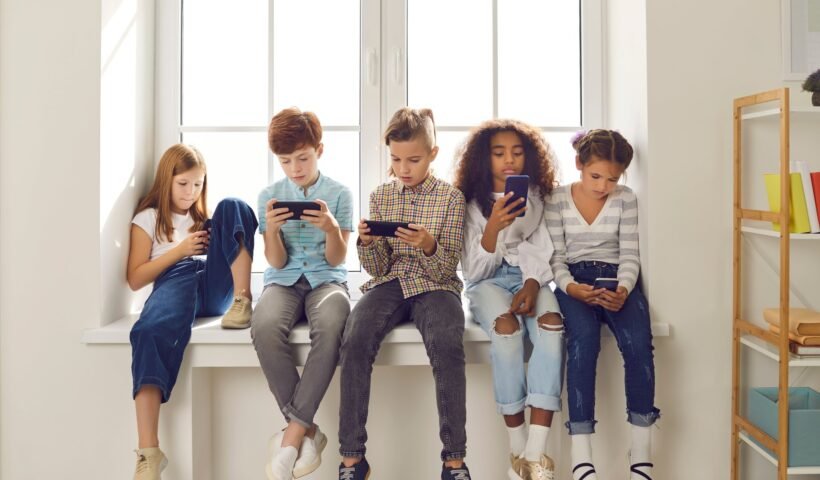 Beş çocuğun pencere kenarında oturup akıllı telefonlarından oyun oynaması