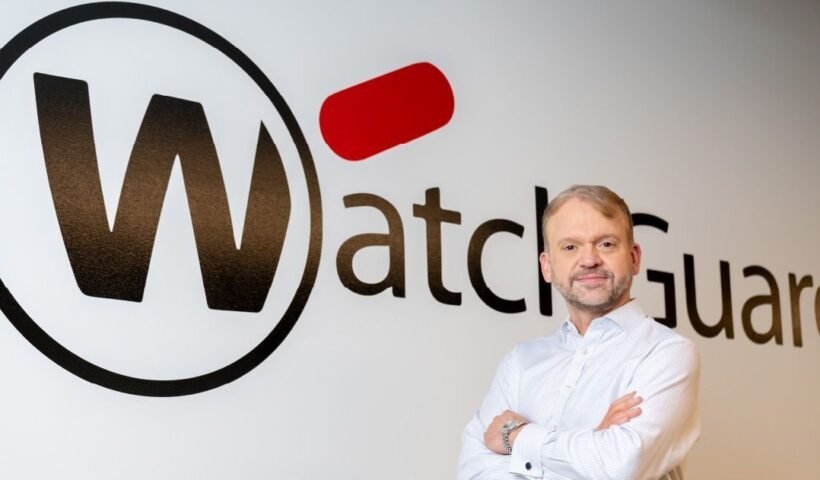 WatchGuard CEO'su Joe Smolarski, şirketin logosunun önünde poz veriyor