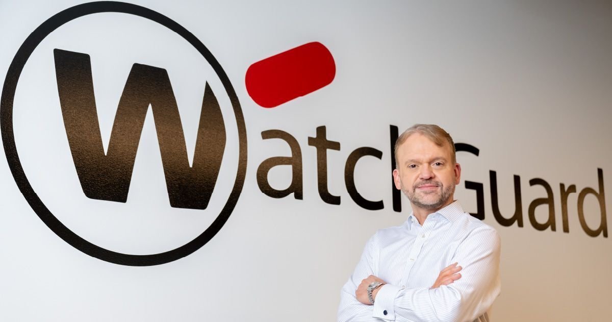 WatchGuard CEO'su Joe Smolarski, şirketin logosunun önünde poz veriyor