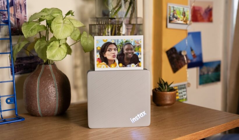 instax Link WIDE 2 yazıcısı bir masanın üzerinde, yeni bastığı WIDE formatlı bir fotoğrafla birlikte
