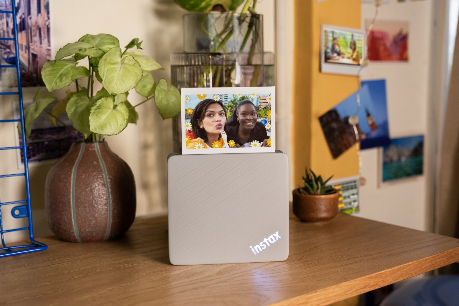 instax Link WIDE 2 yazıcısı bir masanın üzerinde, yeni bastığı WIDE formatlı bir fotoğrafla birlikte